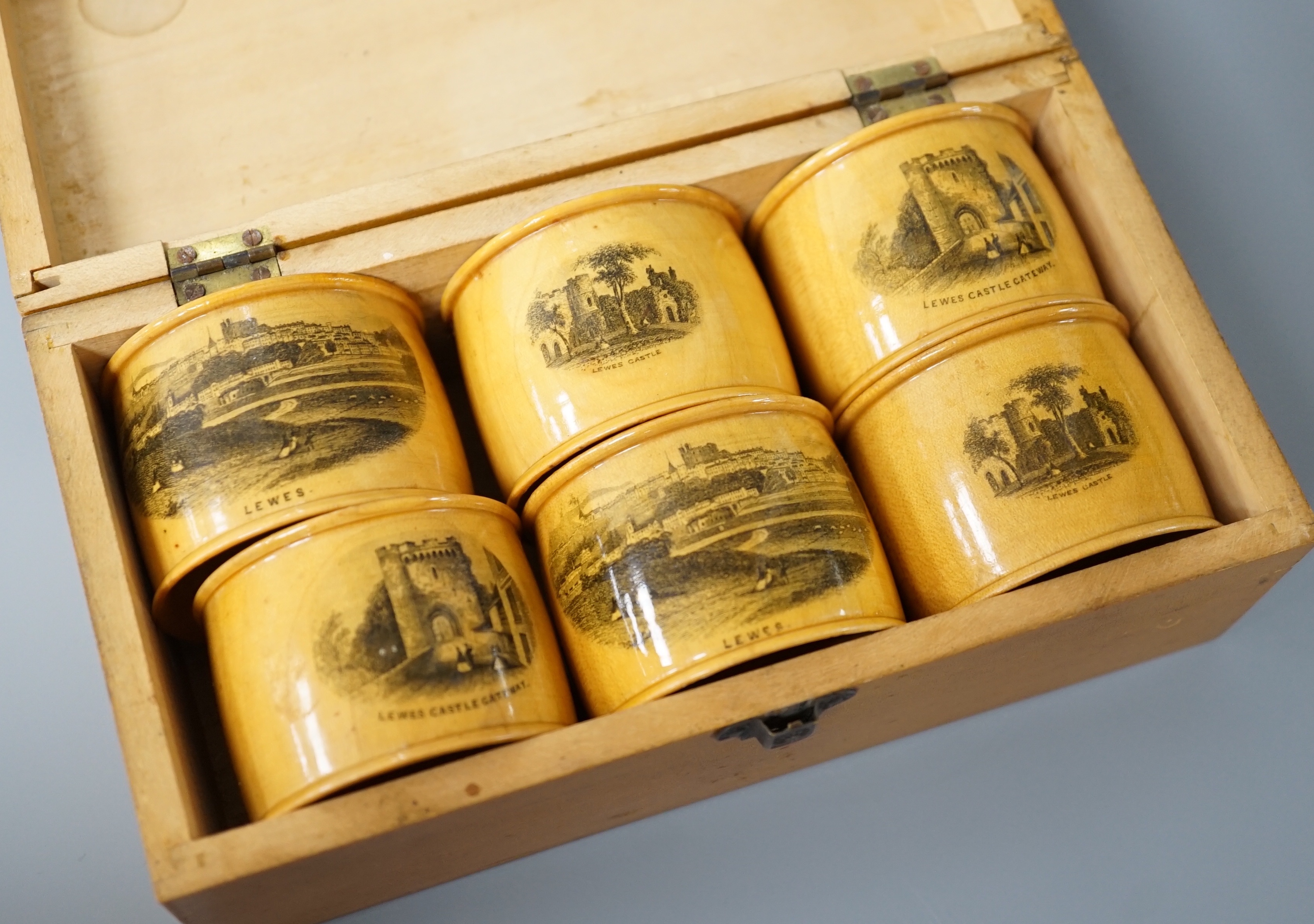 A set of 6 late 19th century mauchline ware napkin rings decorated with scenes of Lewes, housed in matching box. 18cm